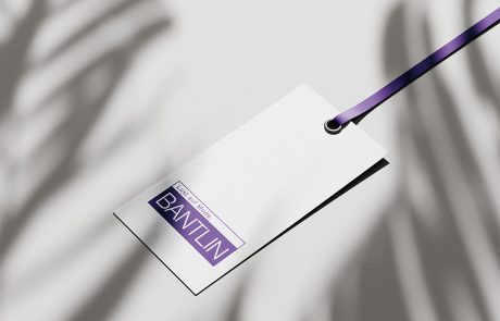 Mockup eines weißen Bantlin-Kleiderlabels mit lila Band und neuem Logoaufdruck, auf hellem Hintergrund.